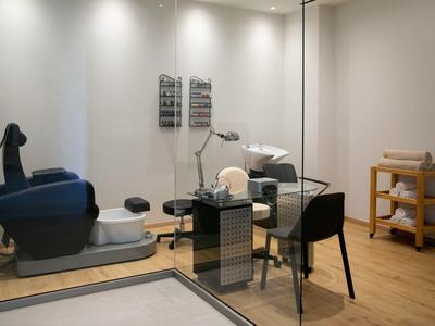 Moderner Behandlungsraum mit Pedikürstuhl, Glaswand und schlichtem Mobiliar.