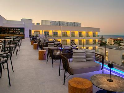Dachterrasse eines Hotels mit Sitzbereichen, Blick auf das Meer bei Sonnenuntergang.