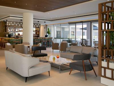 Modern eingerichteter Hotellobby mit Sitzgruppen, Barbereich und großen Fenstern.