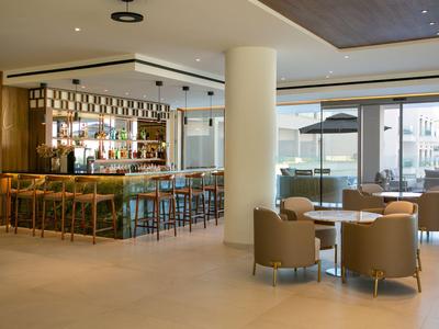 Moderner Hotelbarbereich mit Theke, hohen Stühlen und Sitzbereich mit Sesseln und Tischen.