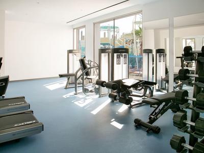 Helles Fitnessstudio mit Geräten, Gewichten, Laufbändern und großem Fenster.