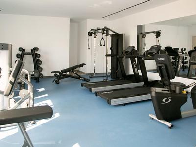 Helle Fitnessraum mit Laufbändern, Kraftgeräten und Klimmzugstange auf blauem Boden.