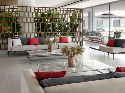 Moderner, heller Lounge-Bereich mit Sofas, Glastischen und Pflanzen als Raumteiler.