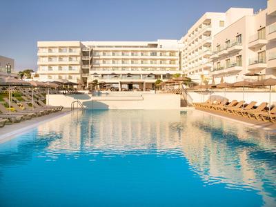 Großes Hotel mit einem Swimmingpool und Sonnenliegen unter klarem Himmel.