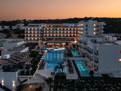 Moderner Hotelkomplex mit beleuchteten Pools und Terrassen bei Sonnenuntergang.