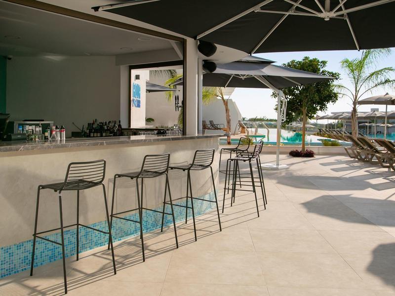 Moderner Außenbarbereich mit Barhockern, Sonnenschirmen und Liegestühlen am sonnigen Pool