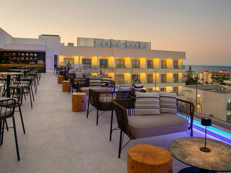 Dachterrasse eines Hotels mit Sitzbereichen und Blick auf das Meer bei Sonnenuntergang.