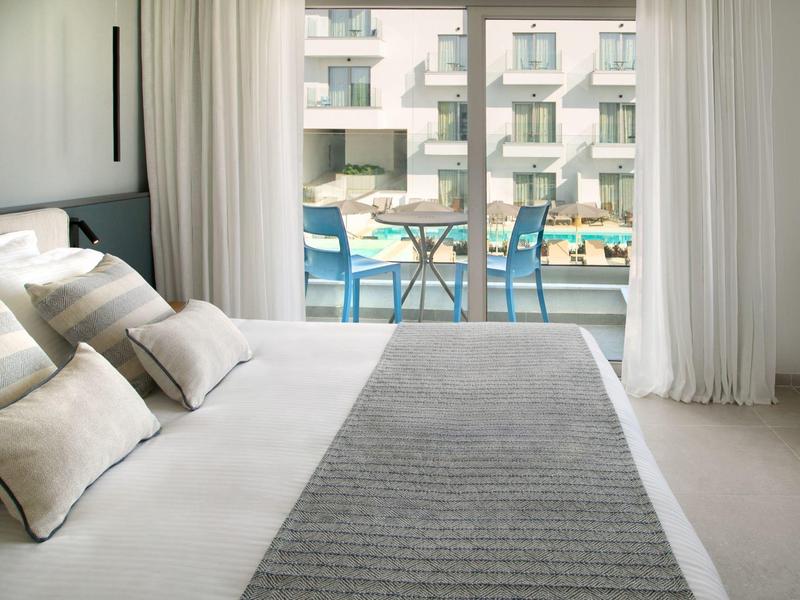 Hell eingerichtetes Hotelzimmer mit großem Bett und Balkon mit Blick auf den Pool.