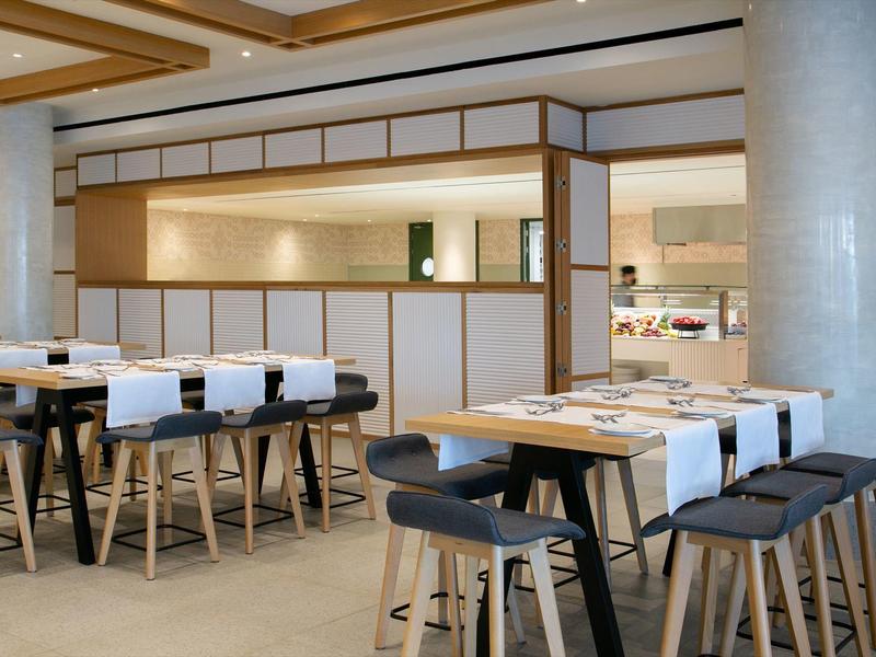 Modernes Restaurant mit Holzstühlen, weißen Tischdecken und heller, offener Raumgestaltung.