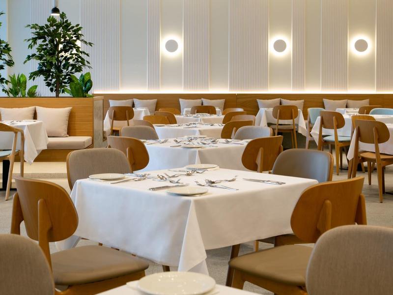 Modern eingerichteter Speisesaal mit weißen Tischdecken und Holzstühlen.