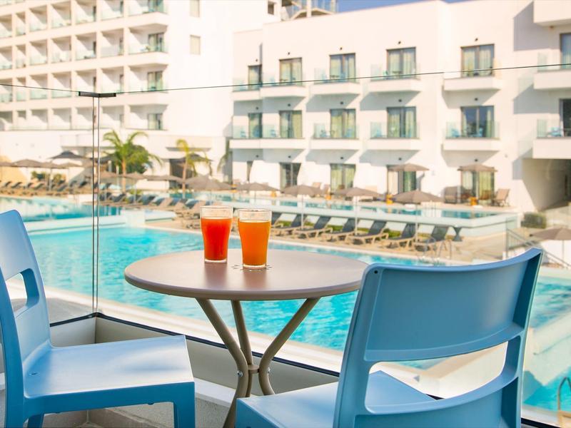 Zwei blaue Stühle und ein Tisch mit zwei Getränken neben einem Hotelpool.