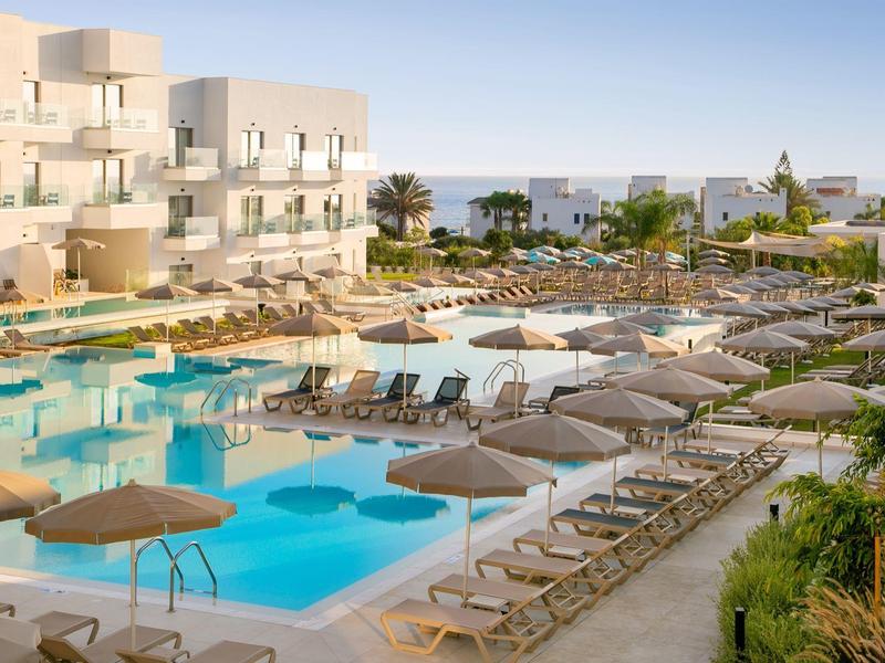 Hotel mit großem Pool und vielen Sonnenliegen unter Sonnenschirmen bei klarem Himmel