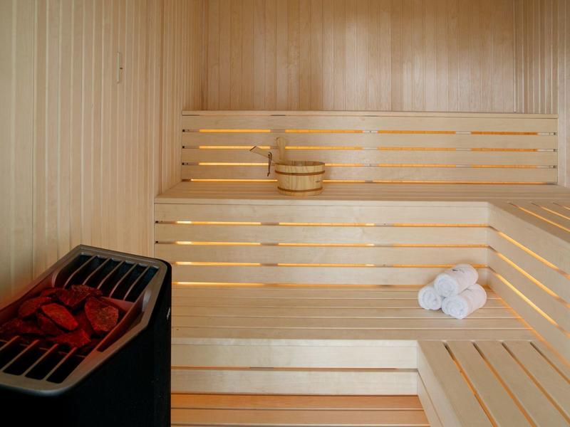 Helle Holzsauna mit mehrstufigen Bänken, einem Saunaofen und weißen Handtüchern.