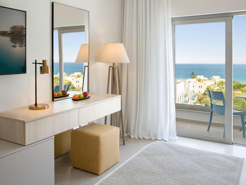 Hell eingerichtetes Hotelzimmer mit Meerblick durch große Fenster und Balkon