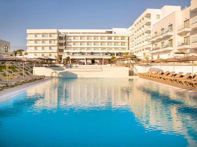 Moderner Hotelkomplex mit großem Außenpool und Liegestühlen bei klarem Himmel.