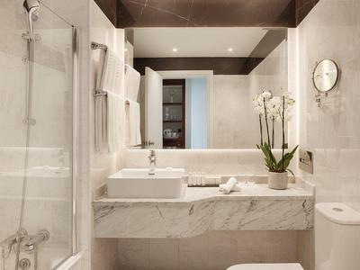 Modernes Hotelbadezimmer mit weißem Waschbecken, großer Spiegelwand und Duschkabine.