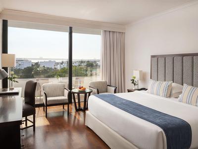 Modernes Hotelzimmer mit großem Bett, Holzboden, Sitzecke und Blick auf Stadt und Meer.