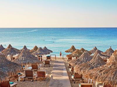 Strand mit Strohhütten, Liegestühlen und ruhigem Meer bei Sonnenuntergang.