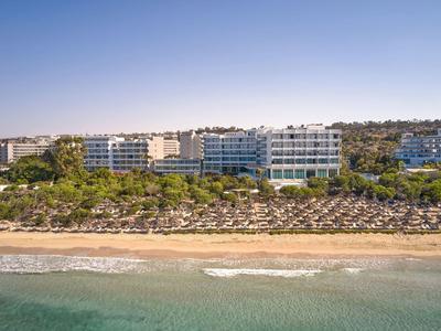 Hotelanlage mit mehreren Gebäuden, Strand und unzähligen Sonnenschirmen an der Küste.