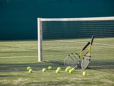 Tennisplatz mit Netz, zwei Tennisschlägern und mehreren Tennisbällen auf dem Gras.