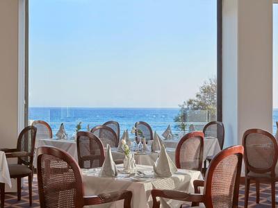 Restaurant mit weißgedeckten Tischen und Meerblick durch große Fenster.