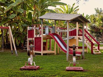 Kinderspielplatz mit Rutsche, Schaukel und Klettergerüst in einem Hotelgarten bei Sonnenschein.