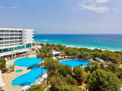 Hotelanlage mit zwei Schwimmbädern, Palmen und Blick auf das blaue Meer und den Strand.