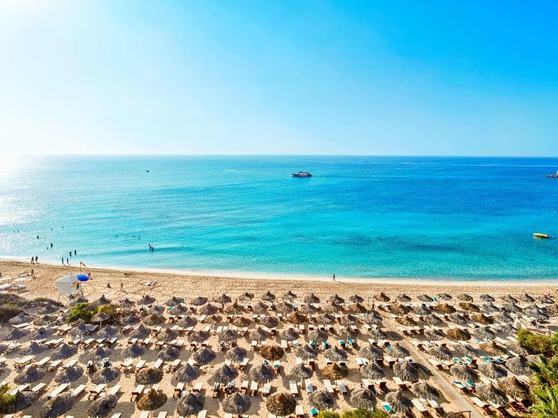 Strand mit Reihen von Sonnenschirmen und Blick auf das ruhige blaue Meer unter blauem Himmel.