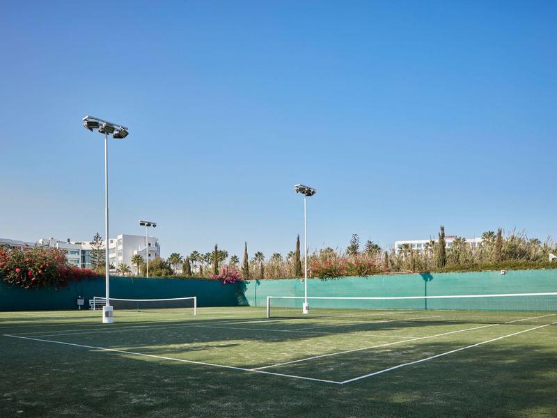Leerer Tennisplatz mit grünem Belag und blauem Himmel im Hintergrund.