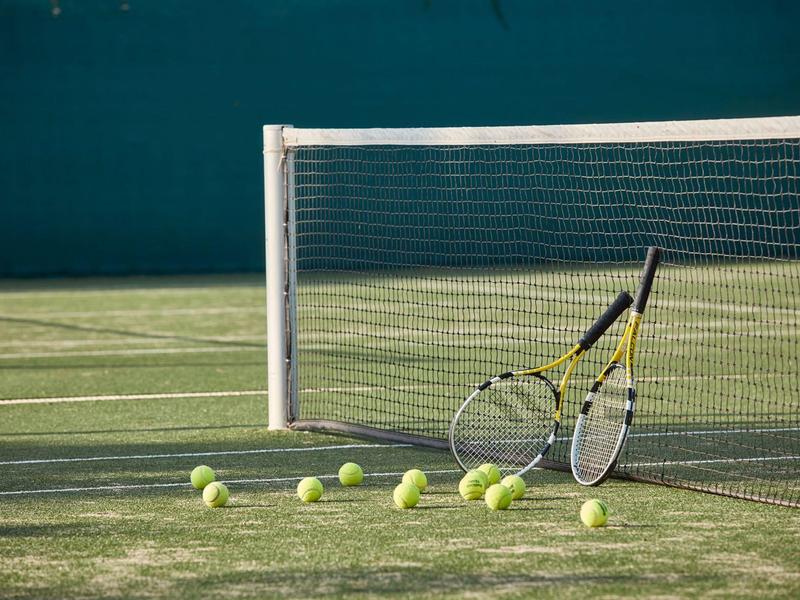 Mehrere Tennisbälle und zwei Tennisschläger lehnen am Tennisnetz auf einem Außenplatz.