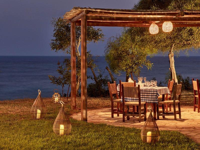 Gemütlicher Außenbereich mit gedecktem Tisch und Laternen am Meer bei Dämmerung.