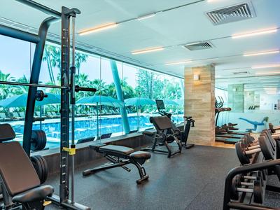 Moderner Fitnessraum mit Geräteausstattung und großen Fenstern mit Blick auf Palmen.