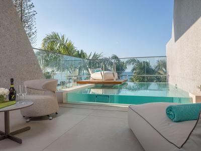Moderner Hotelbalkon mit Pool und Lounge-Möbeln, umgeben von Glasgeländer und tropischer Vegetation.