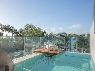 Moderner Pool mit Glasumzäunung und Blick auf Palmen und Meer.