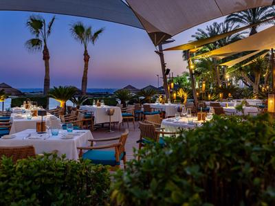 Gemütliches Hotelrestaurant im Freien bei Sonnenuntergang mit Palme und Meerblick.