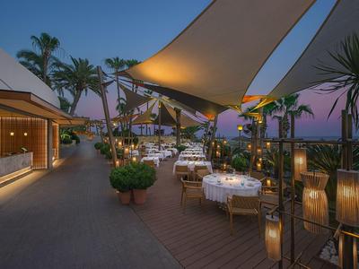 Hotelterrasse bei Dämmerung mit gedeckten Tischen und Palmen.