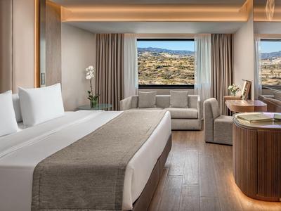 Modernes Hotelzimmer mit großem Bett, Sitzbereich und Blick auf die Landschaft durch bodentiefe Fenster.