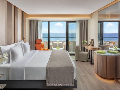 Modernes Hotelzimmer mit Meerblick, großem Bett und Sitzecke am Fenster.