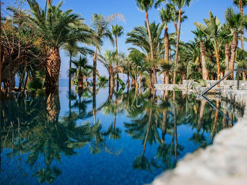 Bazén s čistou vodou a palmami v pozadí pod slunečnou oblohou.