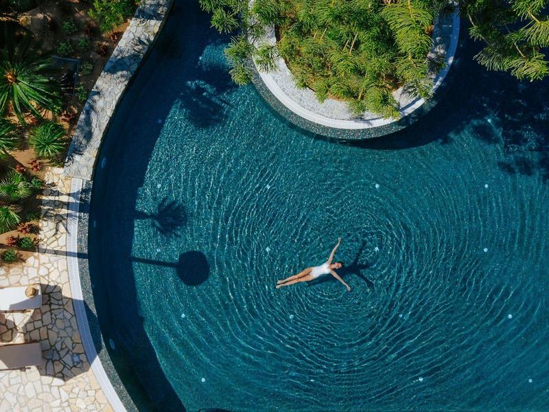 Osoba relaxující se při plavání ve velkém kulatém bazénu obklopeném zahradou.