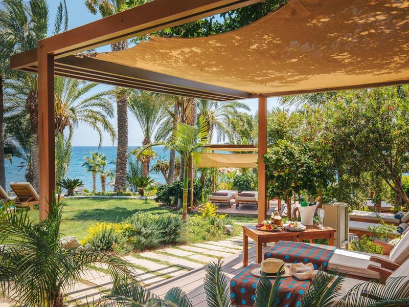 Slunná terasa s odpočinkovým nábytkem a výhledem na palmy a moře.