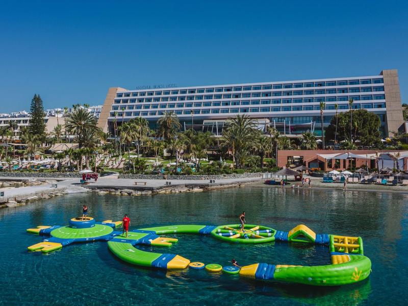 Moderní hotel s velkými skleněnými fasádami, bazénem a nafukovacím vodním parkem.