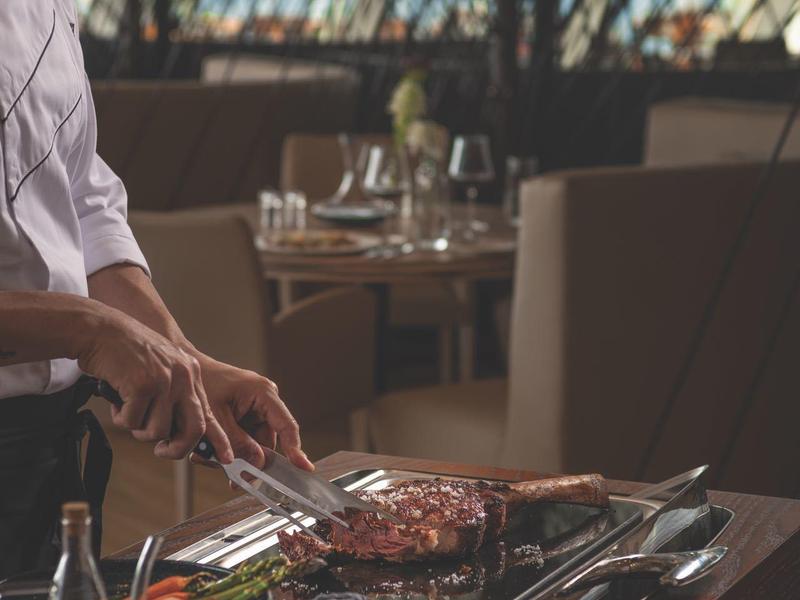 Kuchař připravuje Wagyu steak s omáčkami a bylinkami u stolu v restauraci.