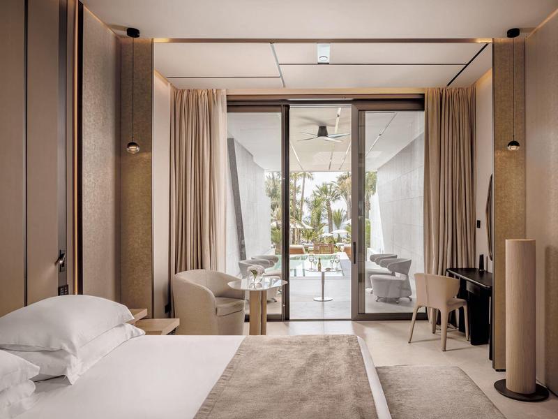 Moderní hotelový pokoj s postelí, židlemi a terasou s výhledem na moře.