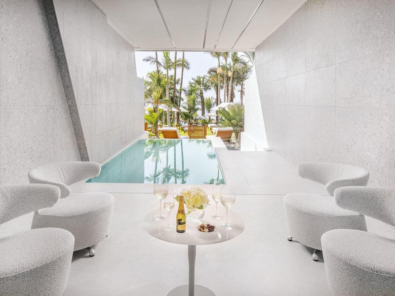 Moderní wellness prostor s bazénem, posezením a výhledem na palmy venku.