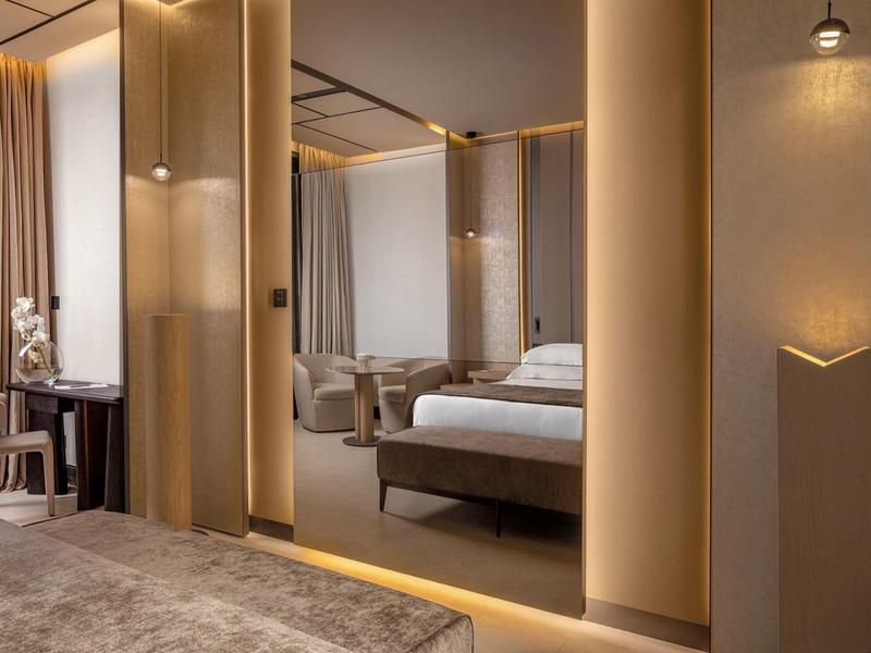 Moderně zařízený hotelový pokoj s velkým zrcadlem, postelí a neutrálními barvami.