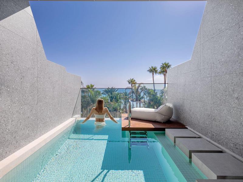 Osoba odpočívající v soukromém bazénu s výhledem na moře a palmy.