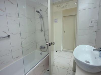 Kleines Badezimmer mit Badewanne, Glasduschwand, weißem Waschtisch und großem Spiegel.