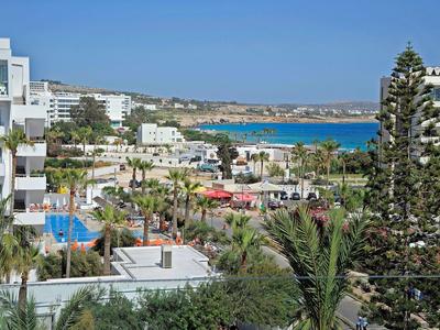 Blick auf Küstenstadt mit weißen Gebäuden, Palmen und blauem Meer bei klarem Himmel.