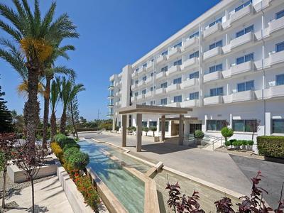 Modern hotel building with outdoor pool, palm trees, and clear blue sky